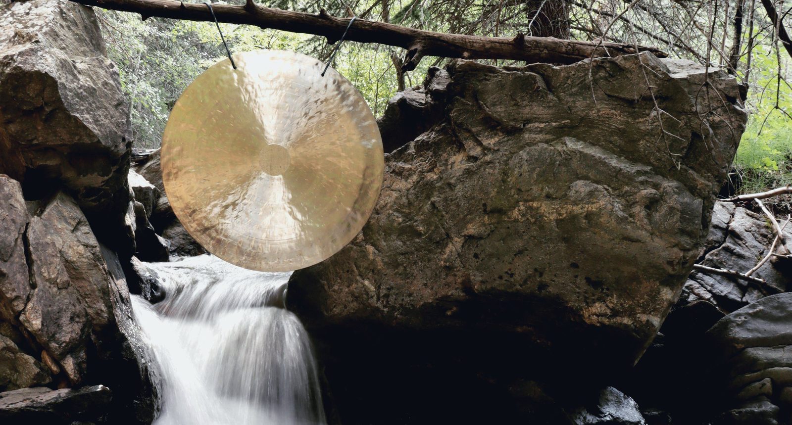 A gong hanging from a branch above a mountain waterfall