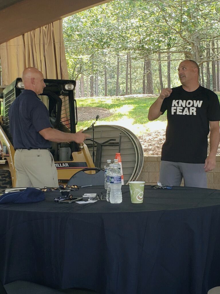 Martyn Church speaking to business owners at a Caterpillar event, wearing a Know Fear shirt
